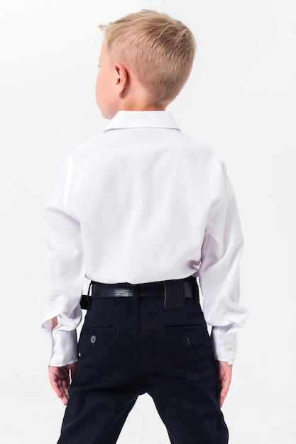 Boy schoolboy posing in a school uniform white shirt and trousers on a white background The boy stands with his back to the camera showing his shirt from behind Vertical photo