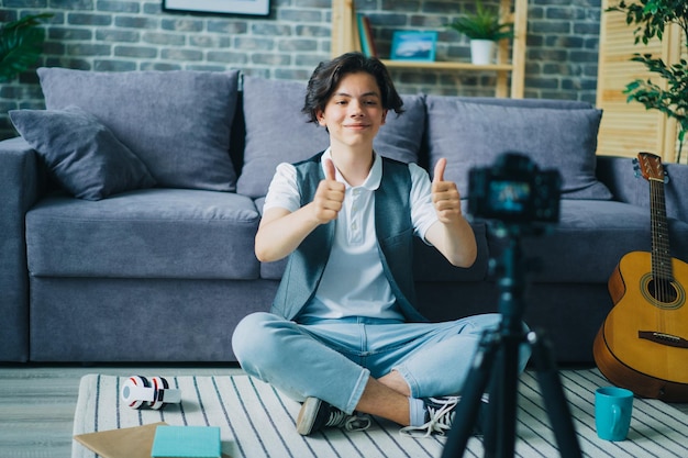 Boy showing thumbsup sitting on floor in front of camera recording video