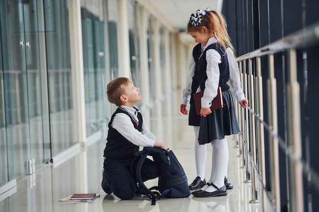 Boy sitting on the floor School kids in uniform together in corridor