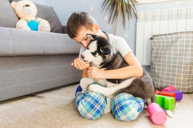 A boy sitting on the floor with his husky puppy