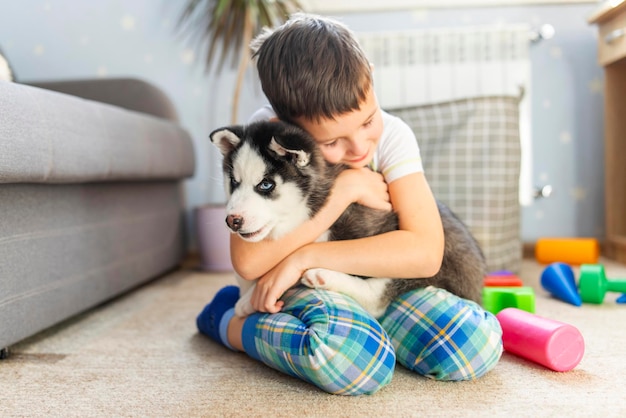 A boy sitting on the floor with his husky puppy