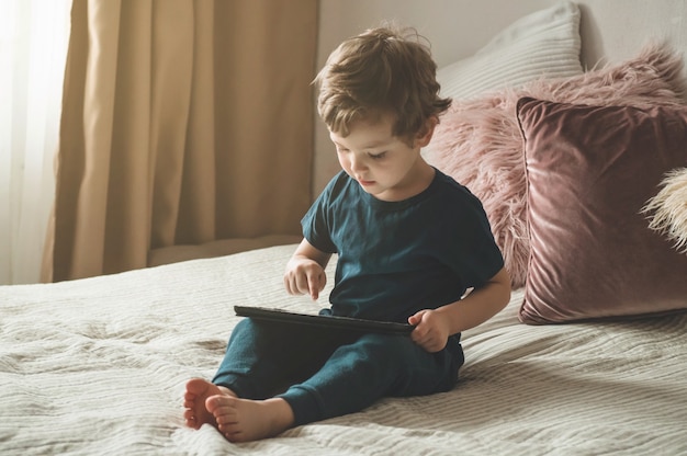 Boy sitting with a tablet on the bed