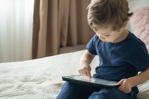 Boy sitting with a tablet on the bed