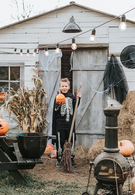 A boy in a skeleton costume on the porch of a house decorated to celebrate a Halloween party