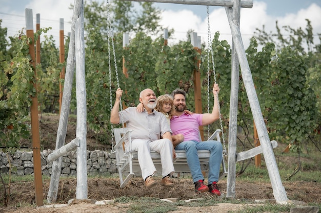 Boy son with father and grandfather swinging together in park outdoors three different generations a