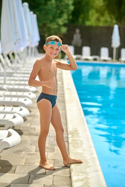 Boy standing near pool gesturing ok