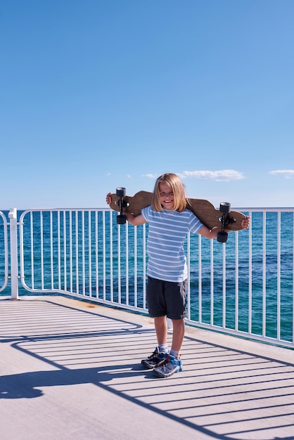 Boy standing with a longboard on a pier at sunny day