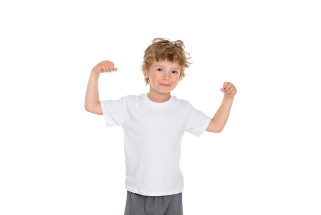 A boy stands on white, raises and bends his arms showing how strong he is