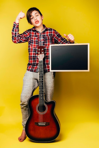 Boy stay with guitar and black board with copy space