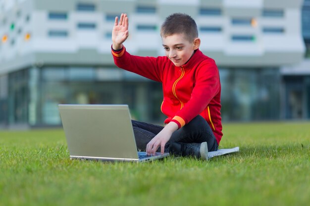 boy a student of  school  sitting on the lawn uses a laptop