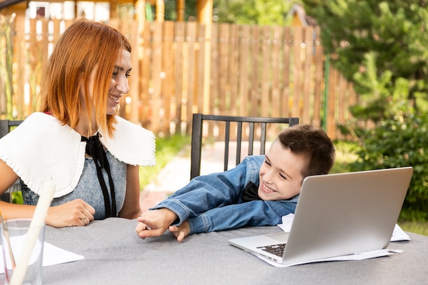 Boy studying from home in an online classroom  in home garden . Schoolboy listens to a lecture and solves problems