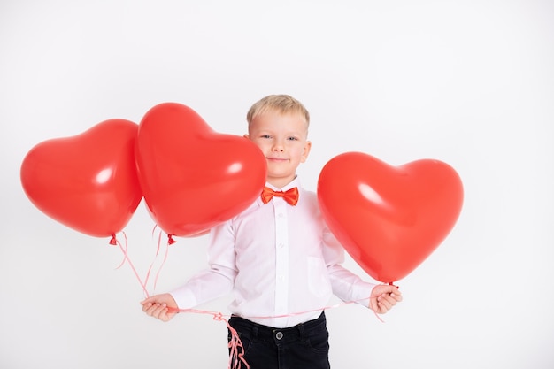 Boy in suit and red bow tie holds heart balloons