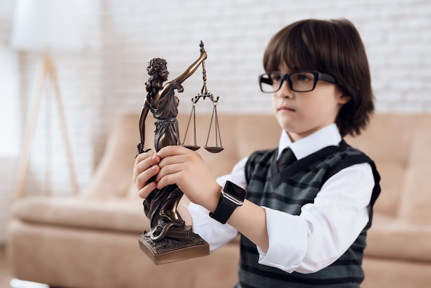 A boy in a suit and tie is holding a figurine of a femida.