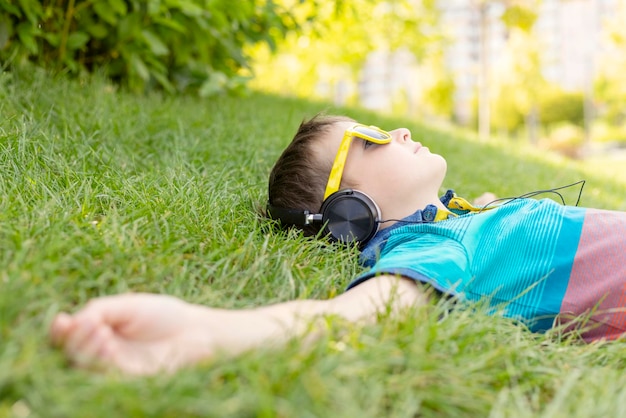 Boy in sunglasses lying on the grass and listening to music in headphones