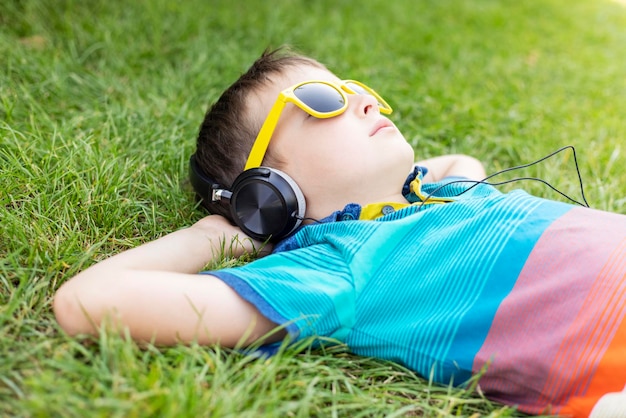 Boy in sunglasses lying on the grass and listening to music in headphones