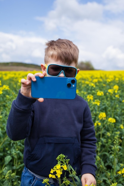 The boy takes pictures of the canola summer landscape on a smartphone