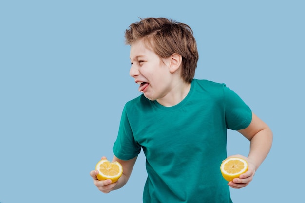 Boy taste a fresh lemon sour taste make grimace facial emotions negative in green tshirt isolated on blue background copy space