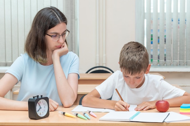 A boy and a teacher doing homework writing text in a notebook at the table A mother helps her son write in a notebook