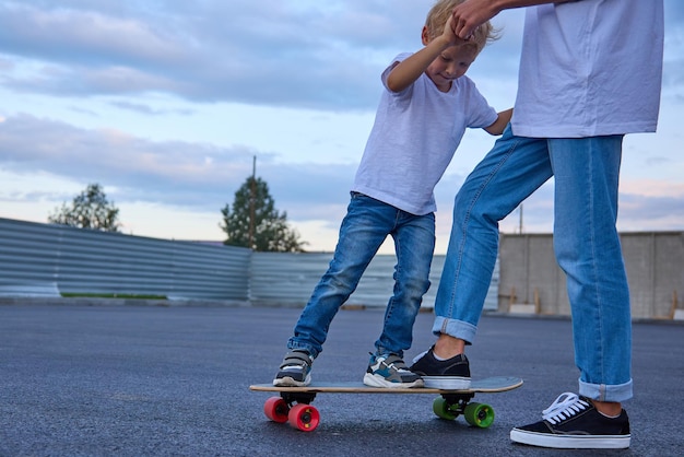 Boy teaches a child to ride a skateboard helps him get on a skateboard