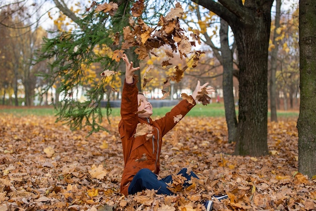 The boy throws autumn yellow leaves that fly at him