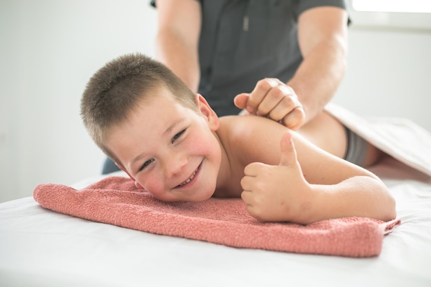 Boy toddler relaxes from a therapeutic massage Physiotherapist working with patient in clinic to treat the back of a child