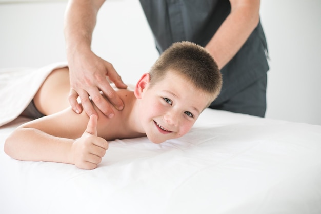 Boy toddler relaxes from a therapeutic massage Physiotherapist working with patient in clinic to treat the back of a child