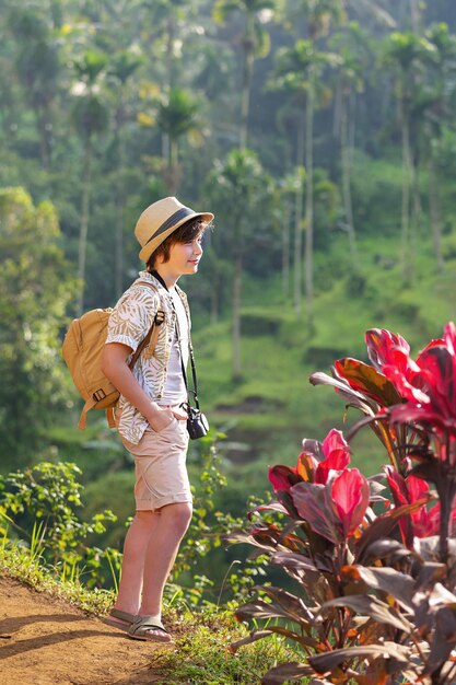 A boy tourist with a backpack and a camera looks at the rice terraces. Bali. Indonesia