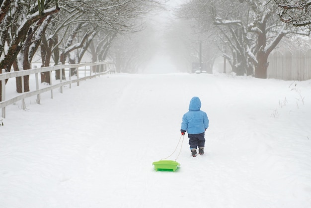 A boy walks home alone and drags his sled behind him