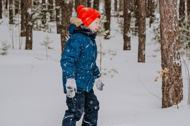 A boy walks in the snow in the winter forest. A child throws snow over his head. Happy winter holidays with snow