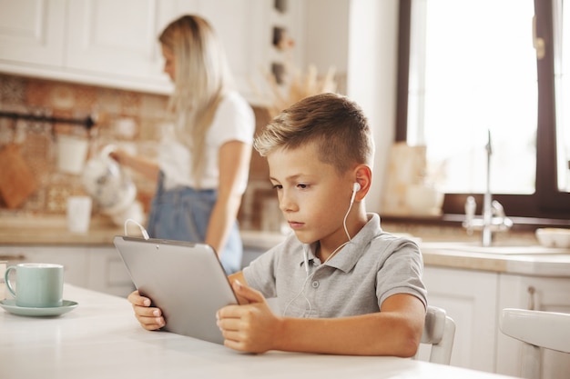 boy watching video on tablet while mom cooks