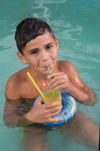 Boy in water drinks a drink from a straw and smiles summer vacation