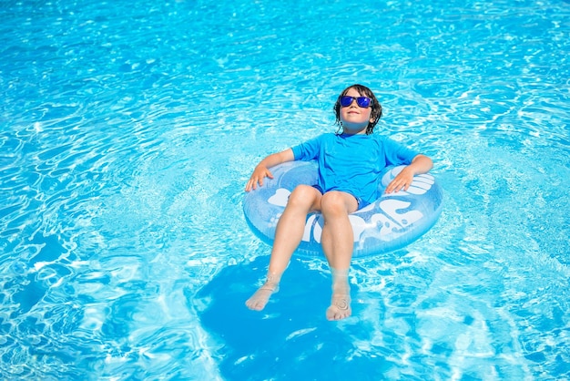 Boy wearing sun glasses relaxing on an inflatable swim ring in a sunny day spending time in a swimming pool aquapark resort hotel Summer holidays concept