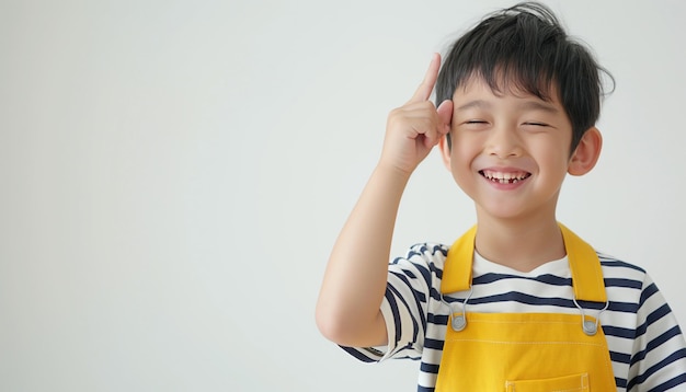 a boy wearing a yellow and white striped shirt is smiling and has his hands up to his ears