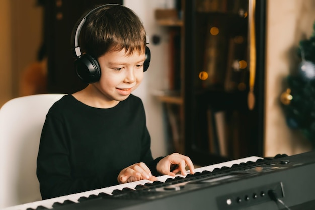 A boy in wireless headphones plays the piano against the background of a Christmas garland