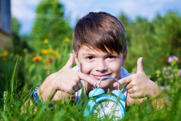 Boy with alarm clock lays in summer garden