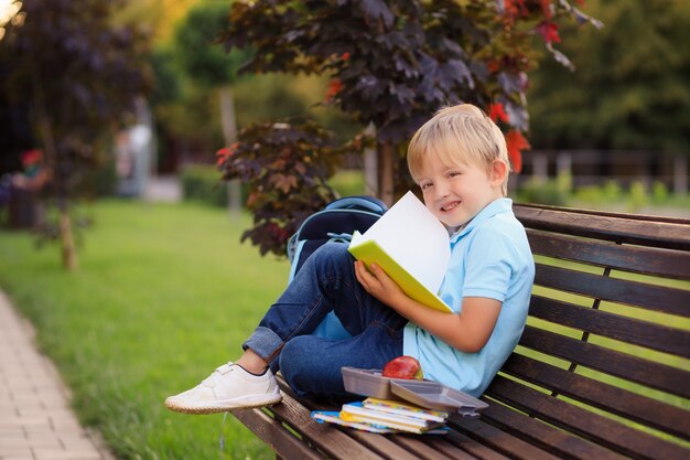 boy with a backpack and books on the first day of school sits in the park.