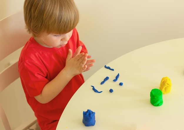 Boy with blond hair and in a red shirt sculpts from plasticine childhood developing activities for children