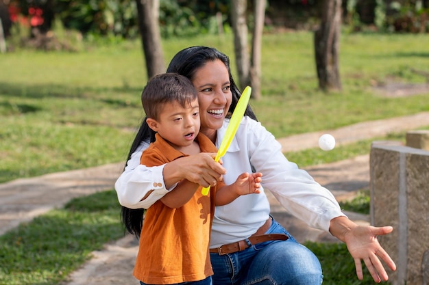 A boy with Down syndrome learns from his mother how to play tennis in a natural park