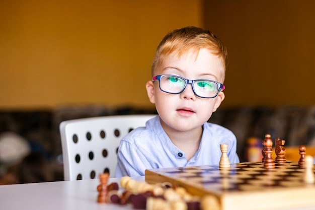 Boy with down syndrome with big glasses playing chess