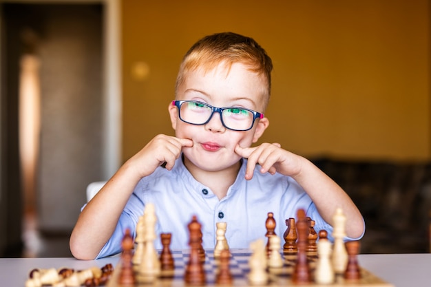 Boy with down syndrome with big glasses playing chess