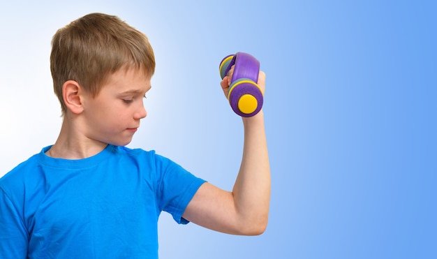 Boy with dumbbells looking at the bicep muscle on blue background