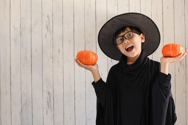 Photo a boy with funny expression wearing halloween costume and holding pumpkins