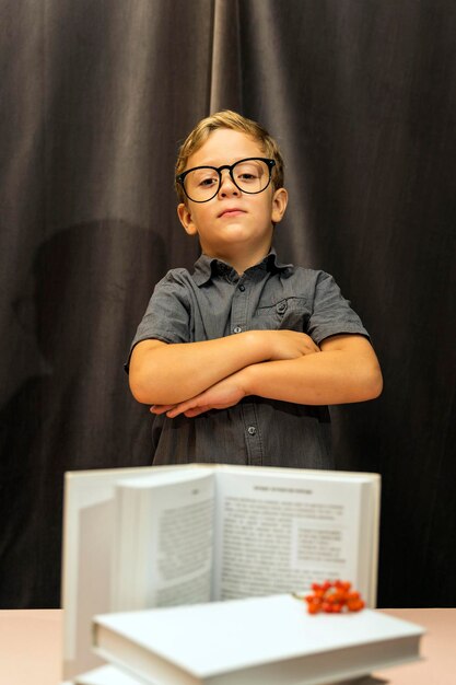 A boy with glasses folded his arms on his chest, a serious look, a stack of books, back to school