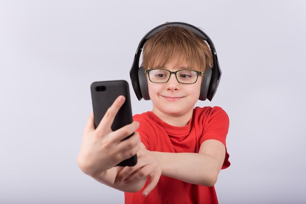 Boy with glasses and headphones with phone in hand Child makes selfie