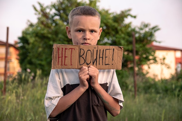 A boy with a grimy face and sad eyes holds a cardboard poster with the inscription NO WAR