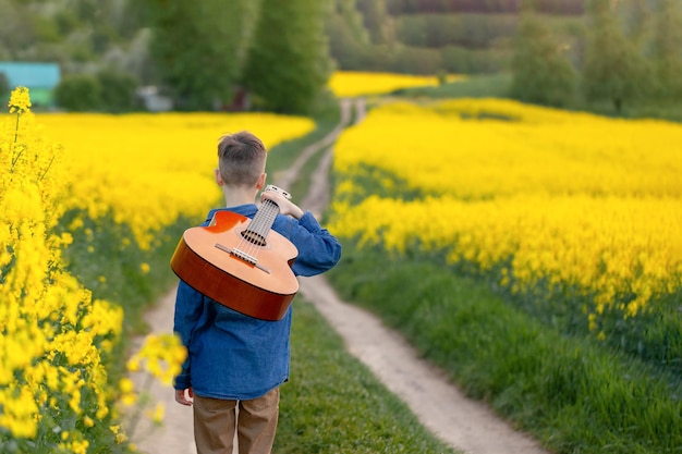 Boy with guitar walking on the summer road. Back view, young musician on the road to success.