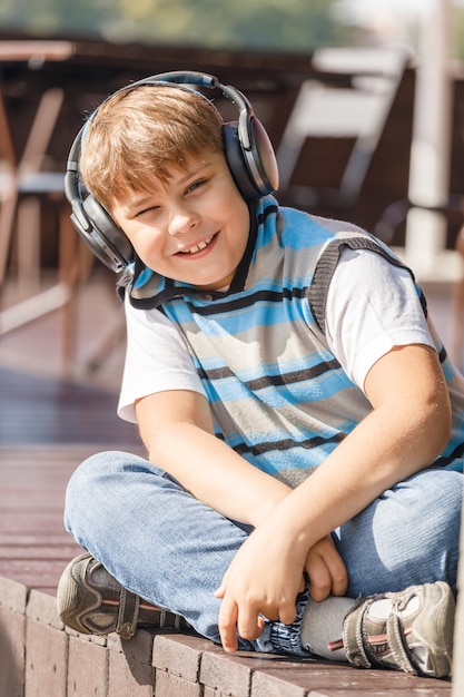 Photo boy with headphones listening to music while sitting on the veranda at home