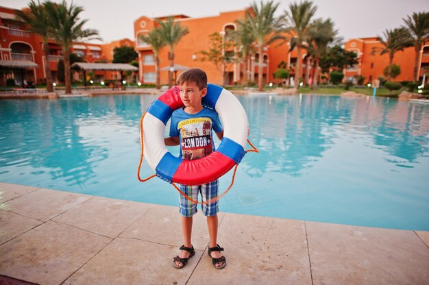 Boy with lifebuoy stand near pool of egyptian resort.