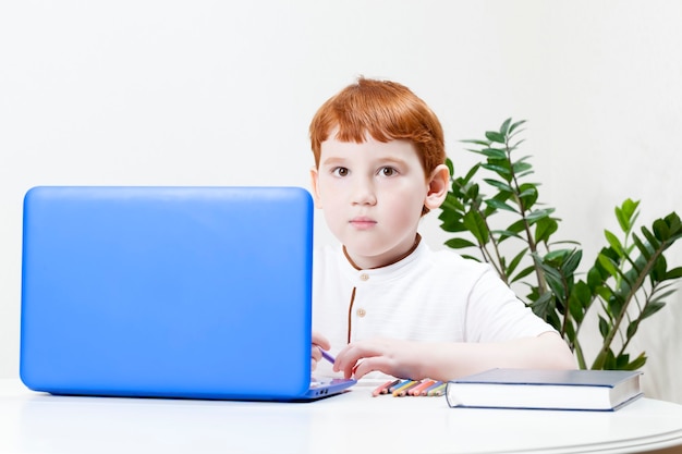 A boy with red hair remotely learns through a computer and the Internet