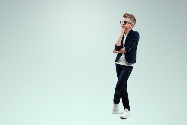 A boy with a suit stands pensive on a white background.